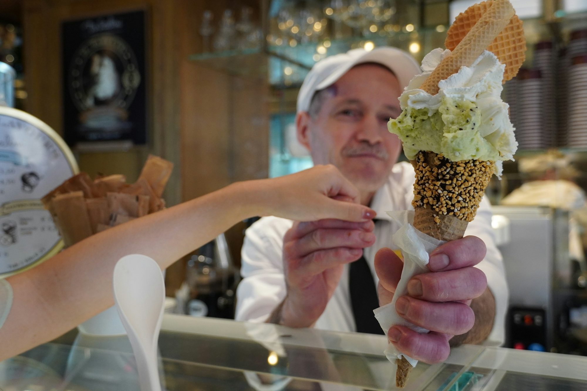 L'intérieur chaleureux d'une gelateria : un glacier tend un grand cornet par-dessus le comptoir